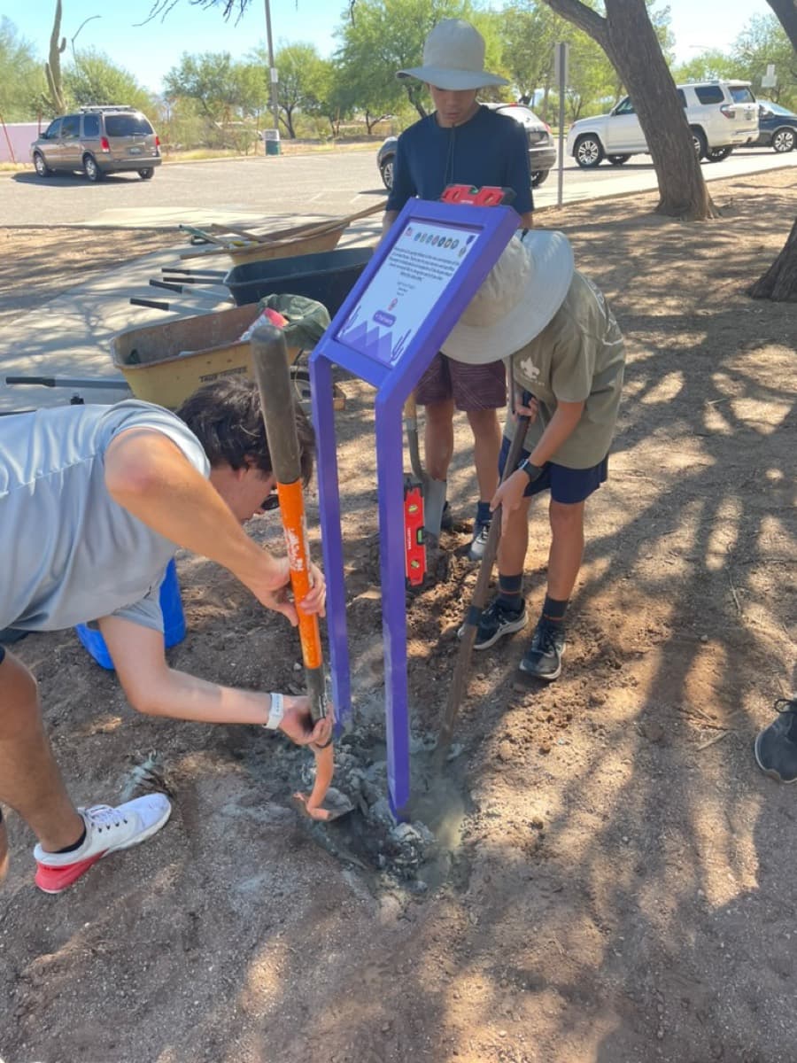 Setting a trail marker post into the ground while two scouts steady it.